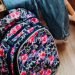 Vibrant floral patterned backpack on a wooden floor beside wooden furniture.