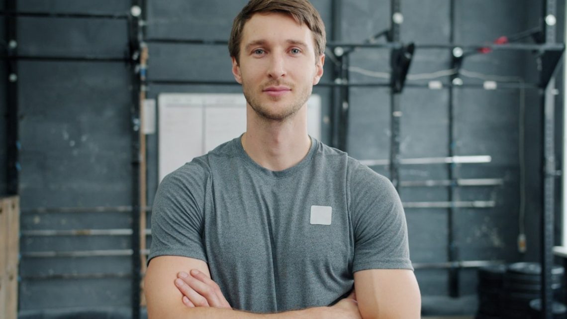 young bodybuilder standing in gym with arms crossed and looking at camera. Healthy youth, bodycare and active lifestyle concept.